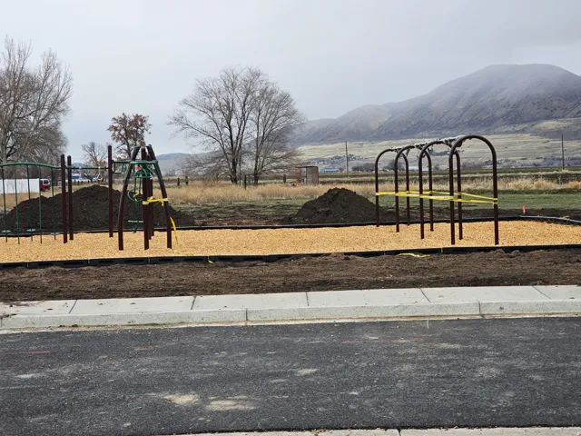 Community playground featuring multiple play structures, a wood chip surface, and a paved street frontage
