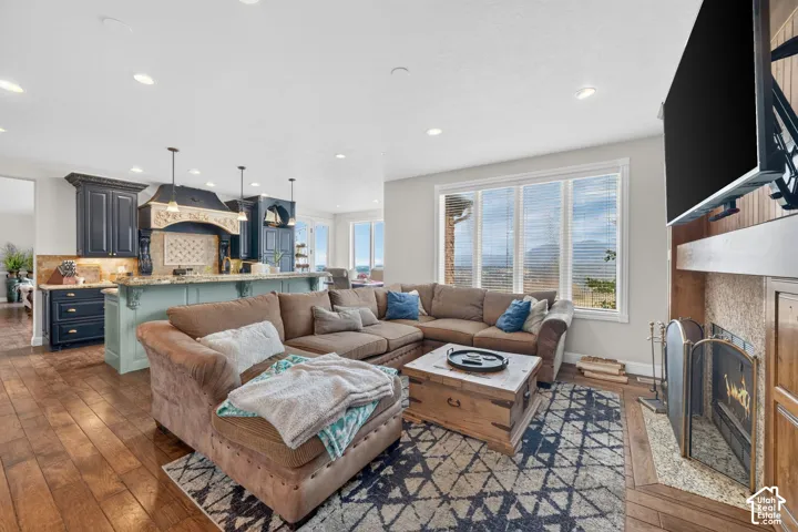 Open-concept living space featuring wood-finish flooring, a stone-surround fireplace with a wood mantel, and large windows