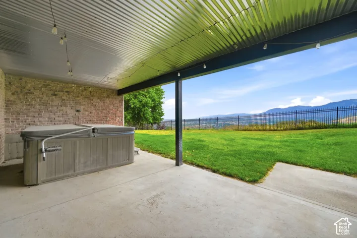 Covered patio featuring a built-in spa with cover, string lighting, concrete flooring, and a corrugated metal ceiling