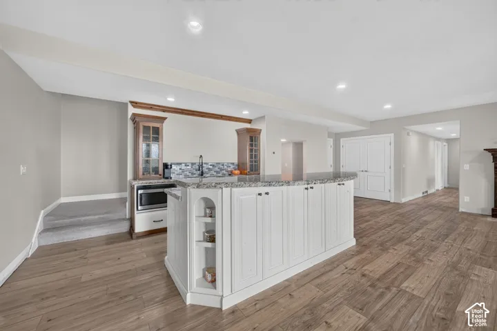 Spacious open-concept area featuring wood-finish flooring, a kitchen island with white cabinetry and an integrated sink, recessed lighting, and a built-in microwave