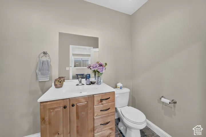 Powder room featuring a wood-finish vanity with a white countertop and integrated sink, a wall-mounted mirror, and dark tile flooring
