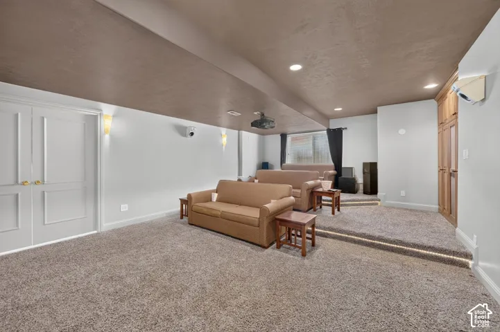 Theater room featuring tiered carpeted flooring, recessed lighting, wall sconces, and built-in wood cabinetry