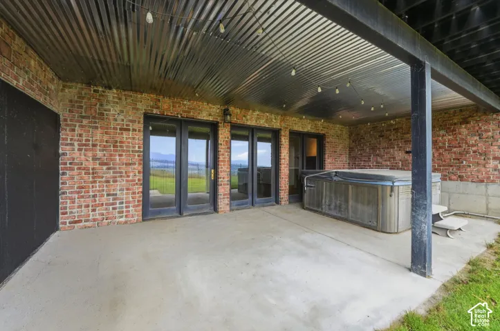 Covered concrete patio featuring a hot tub, string lighting, and brick exterior walls