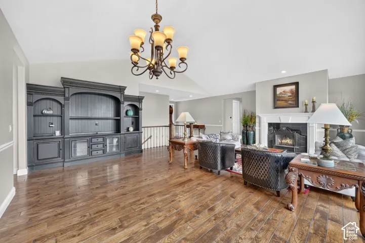 Vaulted ceiling living area featuring wood-finish flooring, a built-in media center, and a fireplace with a white mantel and black surround