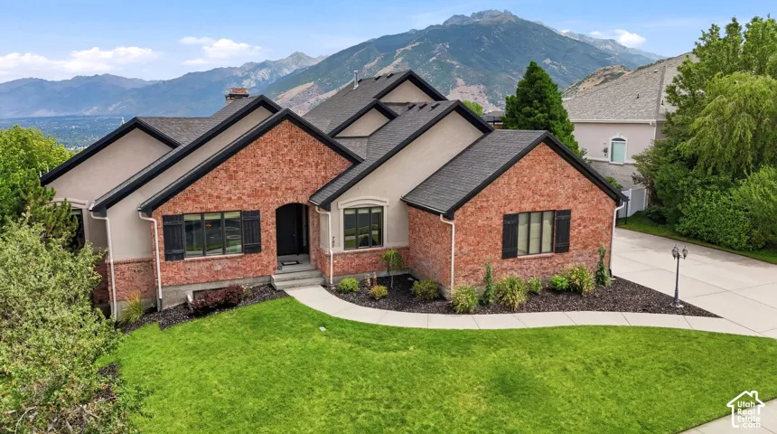 Stately residence featuring a brick and stucco exterior, dark shingle roofing, arched entryway, and front yard landscaping with a curved walkway