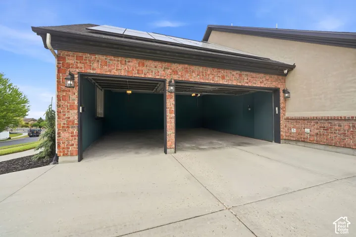 Two-car garage featuring brick exterior accents, solar panels, exterior wall sconces, and a concrete driveway