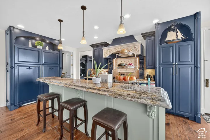 Kitchen featuring wood-finish flooring, a multi-tone granite island countertop, blue cabinetry, recessed lighting, and pendant lighting fixtures