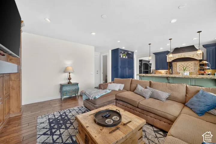 Open-concept living space featuring wood-finish flooring, recessed lighting, and a kitchen with dark blue cabinetry, pendant lighting, and a decorative range hood