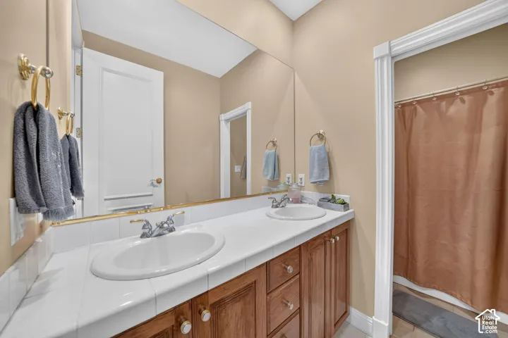 Bathroom featuring a dual-sink vanity with white tile countertop and wood cabinetry