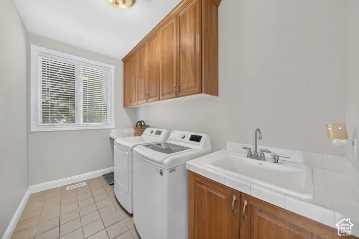 Dedicated laundry room featuring warm wood cabinetry, a utility sink with tiled countertop, and neutral-toned floor tiling