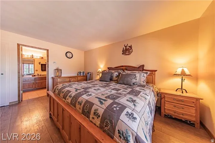 Bedroom featuring wood-finish flooring, a neutral wall color, and an adjoining bathroom with a double vanity