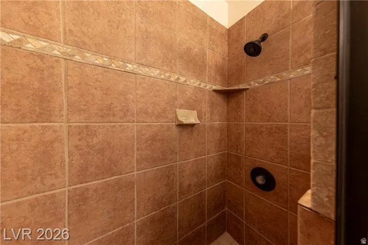 Shower enclosure featuring floor-to-ceiling earth-toned tile, decorative mosaic tile accent band, built-in corner shelf, built-in soap dish, and dark-finish shower fixtures