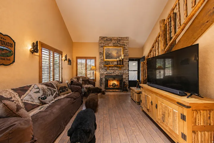 Living area featuring wood-finish flooring, a stone fireplace with a wood mantle, and vaulted ceilings