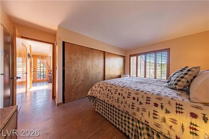 Bedroom featuring wood-finish flooring, a large window with plantation shutters, wood panel closet doors, and light-toned wall finishes