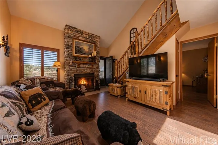 Living area featuring a floor-to-ceiling stone fireplace, wood-finish flooring, and a rustic wood staircase