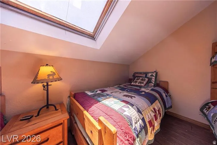 Sloped ceiling room featuring a skylight, wood-finish flooring, and a wooden bed frame