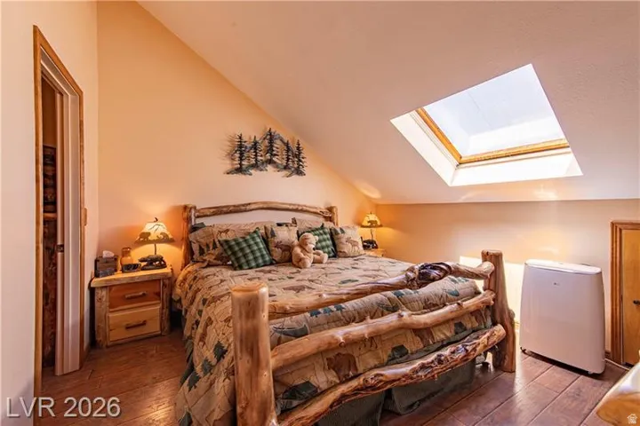Sloped ceiling room featuring a skylight, wood-finish flooring, and a natural wood bed frame