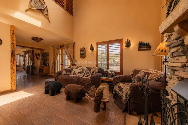 Spacious living area featuring wood-finish flooring, a stacked stone fireplace, and wood-shutter windows