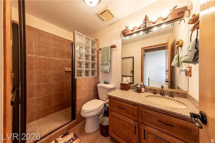 Bathroom featuring a tiled walk-in shower with glass block accent, wood-finish vanity with granite-style countertop, and decorative vanity lighting
