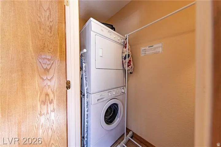 Dedicated utility space featuring a stacked washer and dryer, wood-finish flooring, and a wall-mounted clothes rack