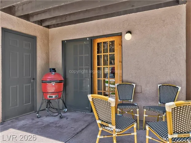 Covered outdoor patio featuring a wood-frame glass panel door, gray panel door, stucco exterior, and overhead wood beams