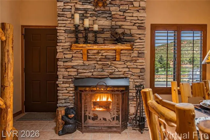 Stacked stone fireplace with a rustic wood mantel, detailed metal fire screen, tile flooring, and a paneled wood entry door