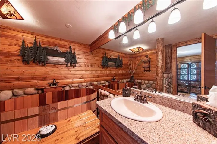 Bathroom featuring a built-in wooden soaking tub, wood-panel walls, and a vanity with a granular countertop