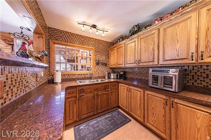 Kitchen featuring warm wood cabinetry, mosaic tile backsplash, a stainless steel sink, and ample counter space