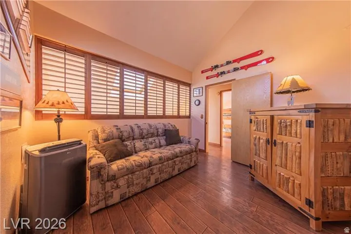 Living area featuring wood-finish flooring, a vaulted ceiling, and a large window with plantation shutters