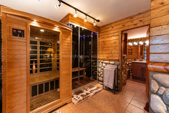 Built-in sauna with wood paneling and a glass door, custom glass-enclosed shower, natural wood paneling, river rock accents, and durable tile flooring