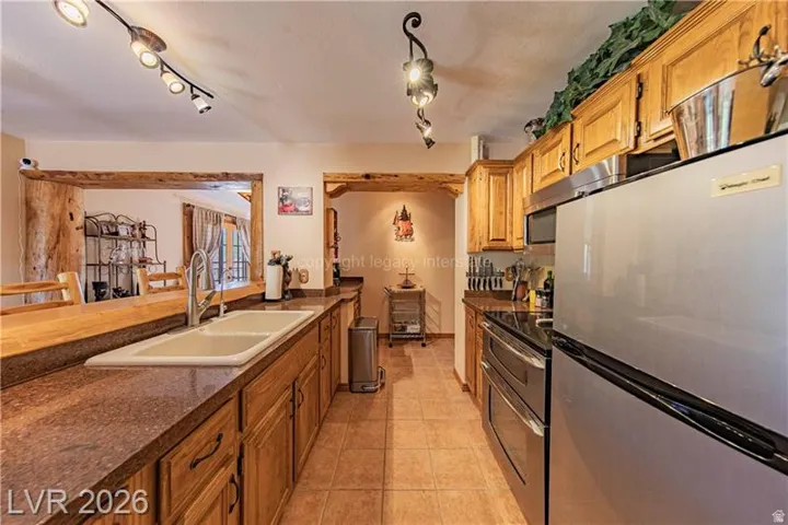 Kitchen featuring wood-finish cabinetry, stainless steel appliances, a double basin sink, and tiled flooring
