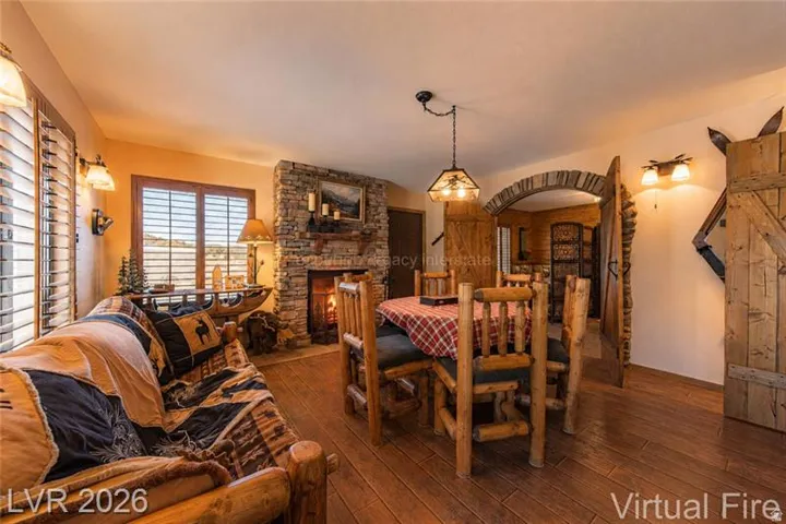 Open-concept living and dining area featuring wood-finish flooring, a stone-clad fireplace with a hearth and mantel, and multiple windows with plantation shutters