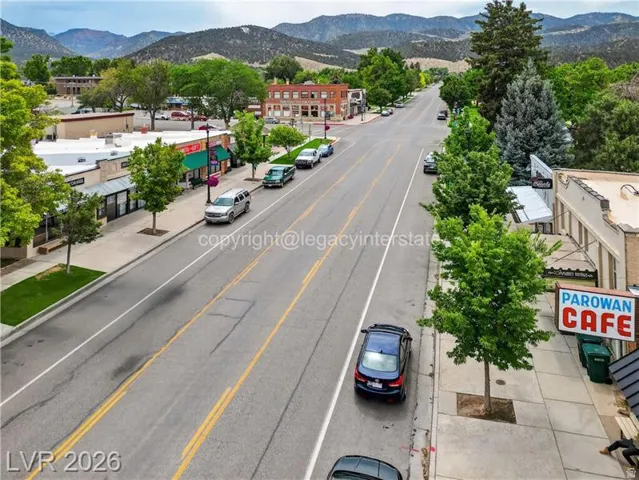 Commercial streetscape featuring brick and stucco buildings, mature street trees, and a mountain backdrop
