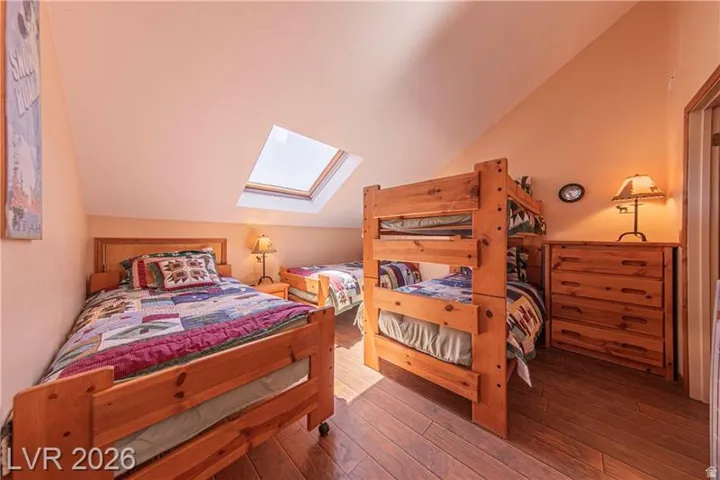 Attic bedroom featuring a prominent skylight, sloped ceilings, wood-finish flooring, a wood bunk bed, and a wooden dresser