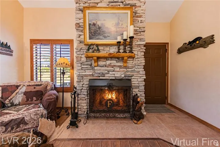 Stacked stone fireplace with a rustic wood mantel, wrought iron fire screen, and tile hearth