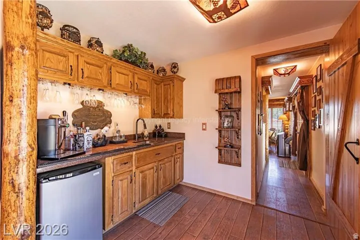 Wet bar featuring wood-finish cabinetry, dark countertop, and under-cabinet glass racks