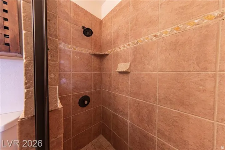Tiled shower enclosure featuring a dark bronze shower head and control, an integrated corner shelf, a built-in soap dish, and decorative accent tiling