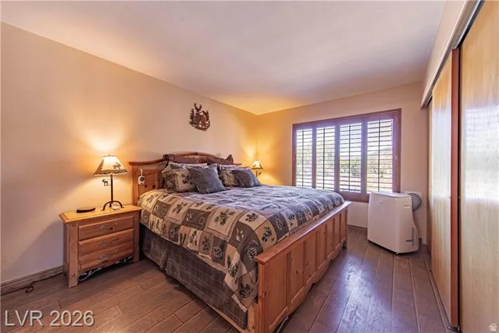 Bedroom featuring wood-finish flooring, a window with plantation shutters, and light wood-tone sliding closet doors
