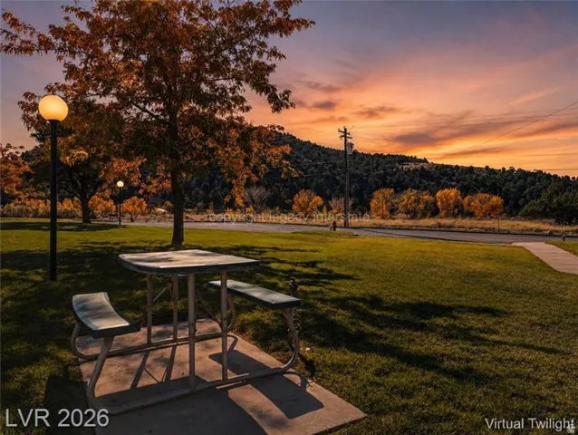 Park-like setting featuring a picnic table on a concrete pad, mature trees with autumn foliage, and a paved walking path