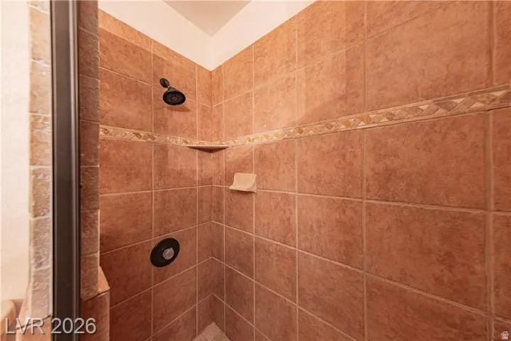 Tiled shower enclosure featuring a dark bronze showerhead, an integrated soap dish, and two corner shelves