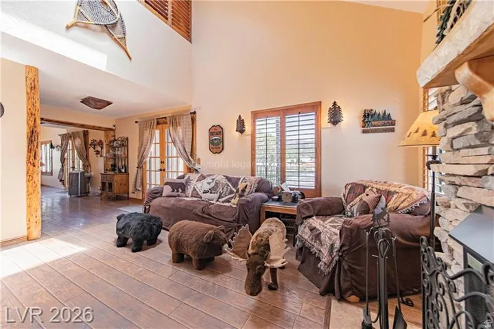 Spacious living area featuring wood-finish flooring, a stacked stone fireplace with hearth, and high ceilings