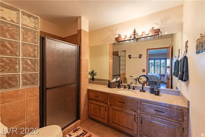 Bathroom featuring a glass block shower enclosure, textured glass shower door, and a single vanity with wood cabinetry and a speckled countertop
