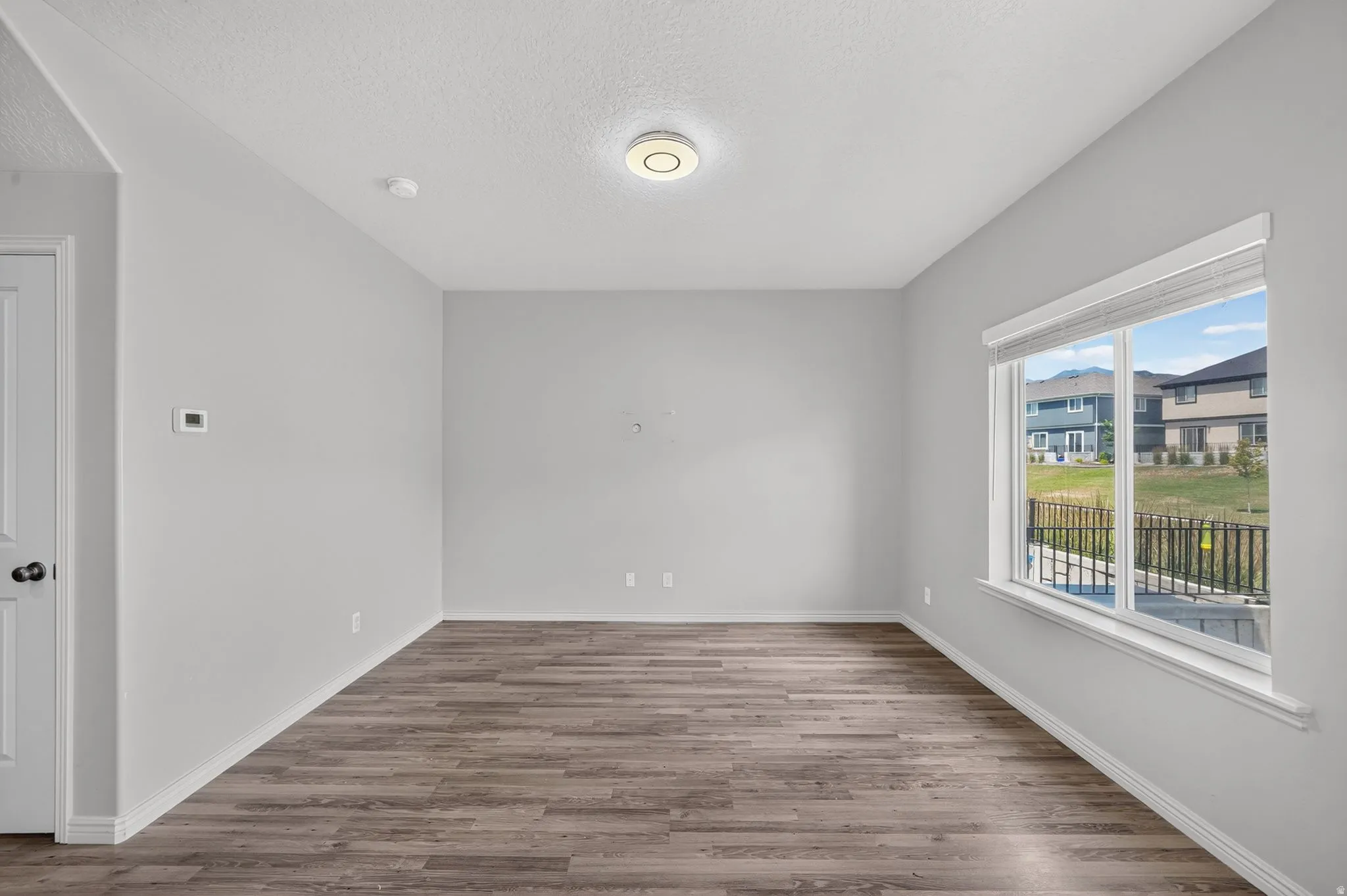 Spacious room featuring wood-finish flooring, a large window with blinds, and contemporary lighting
