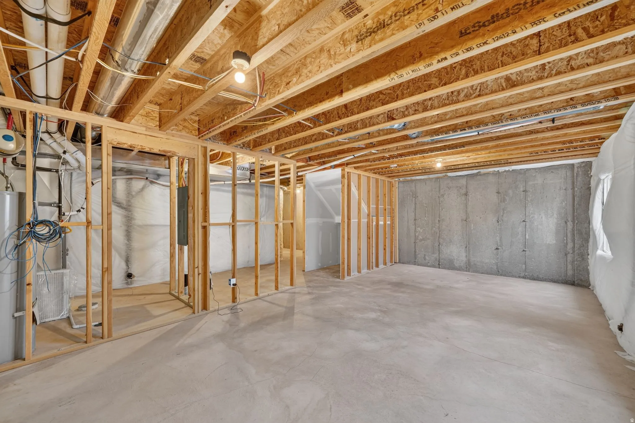 Unfinished lower level featuring concrete flooring, exposed wood joists, framed interior walls, and an accessible water heater