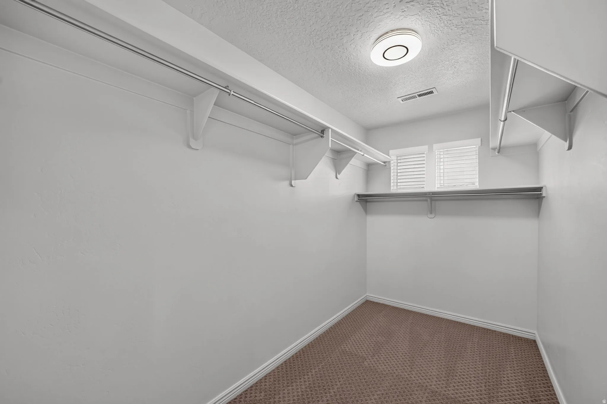 Walk-in closet featuring built-in shelving, hanging rods, and twin windows with horizontal blinds