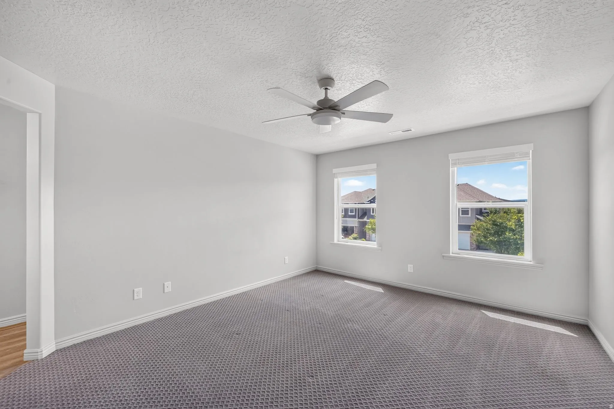Spacious room featuring neutral carpeting, two windows with white trim, and a ceiling fan