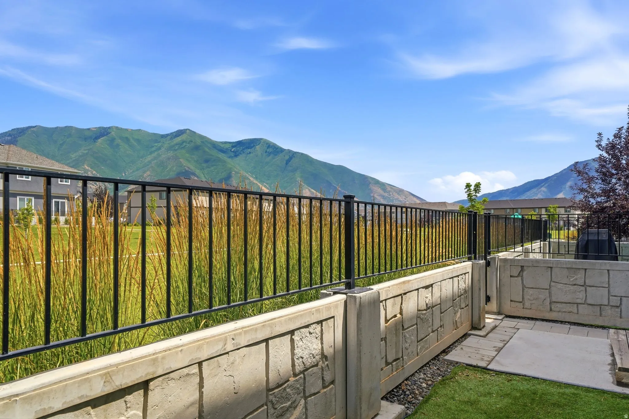 Expansive outdoor space featuring a stone-faced retaining wall, black metal fencing, and a concrete patio area