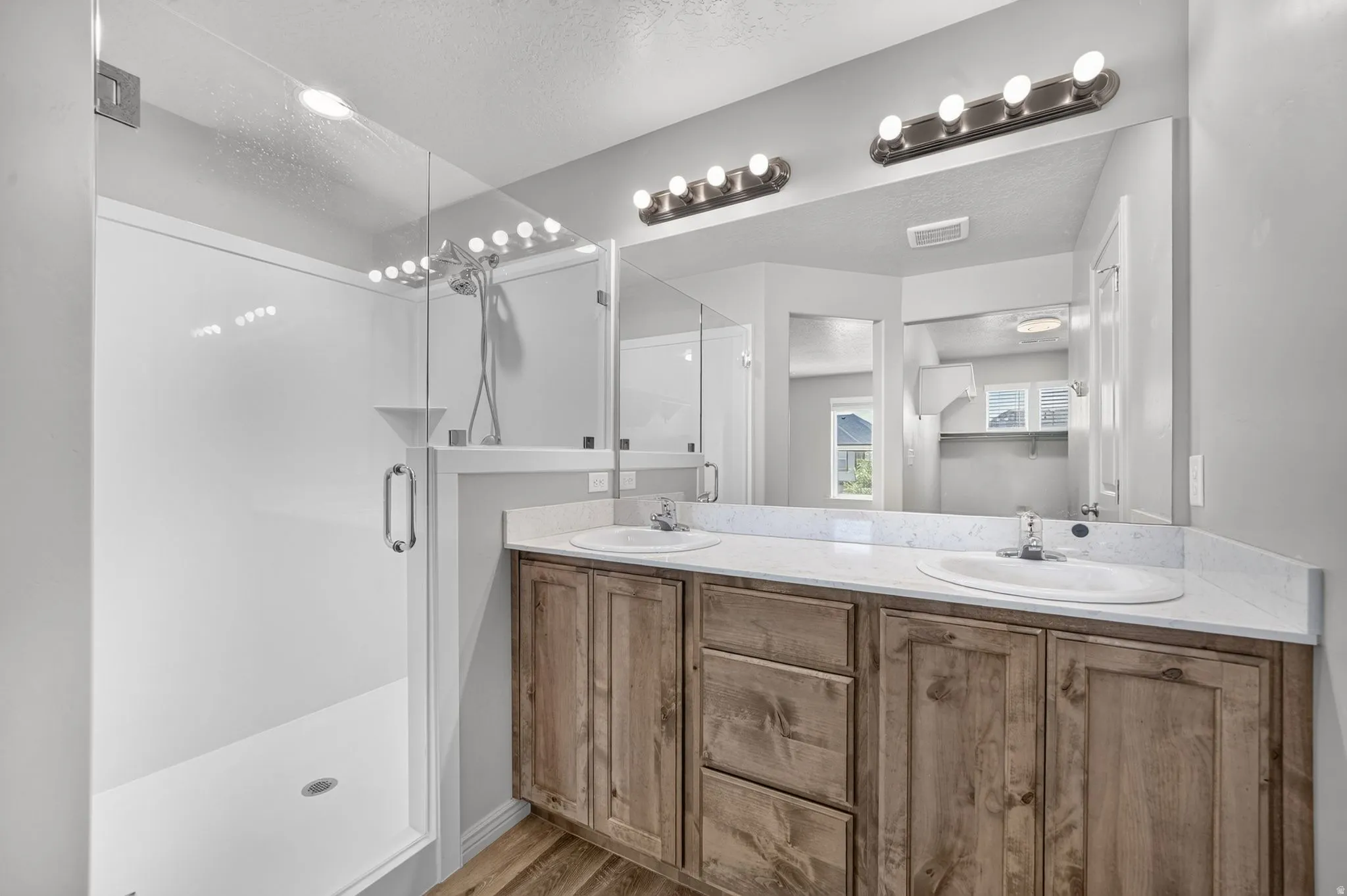 Bathroom featuring a dual vanity with wood-finish cabinetry and white countertops, individual sinks with chrome faucets, and a large mirror with dual overhead light fixtures
