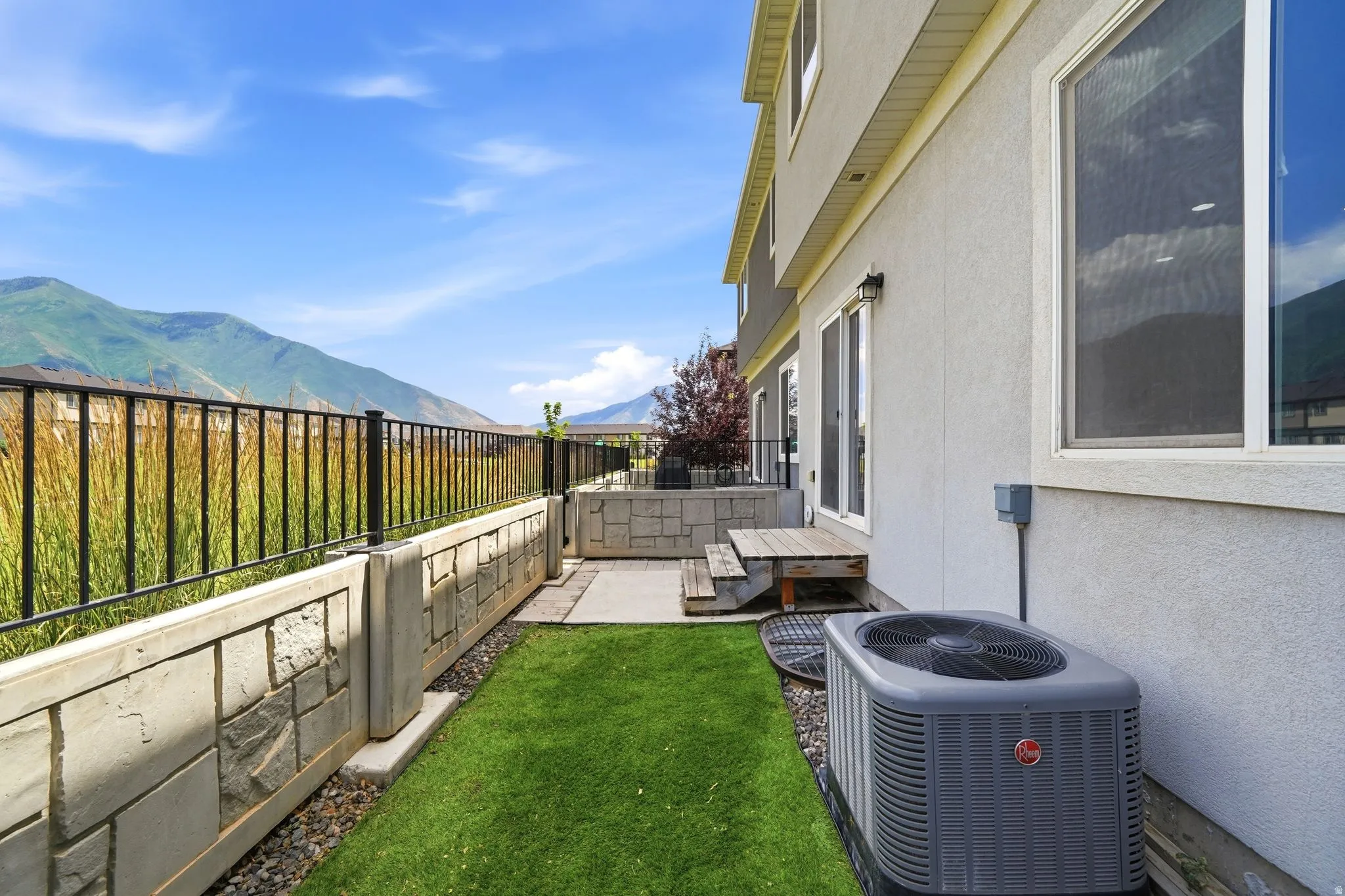 Backyard area with a retaining wall, black metal fencing, and green turf