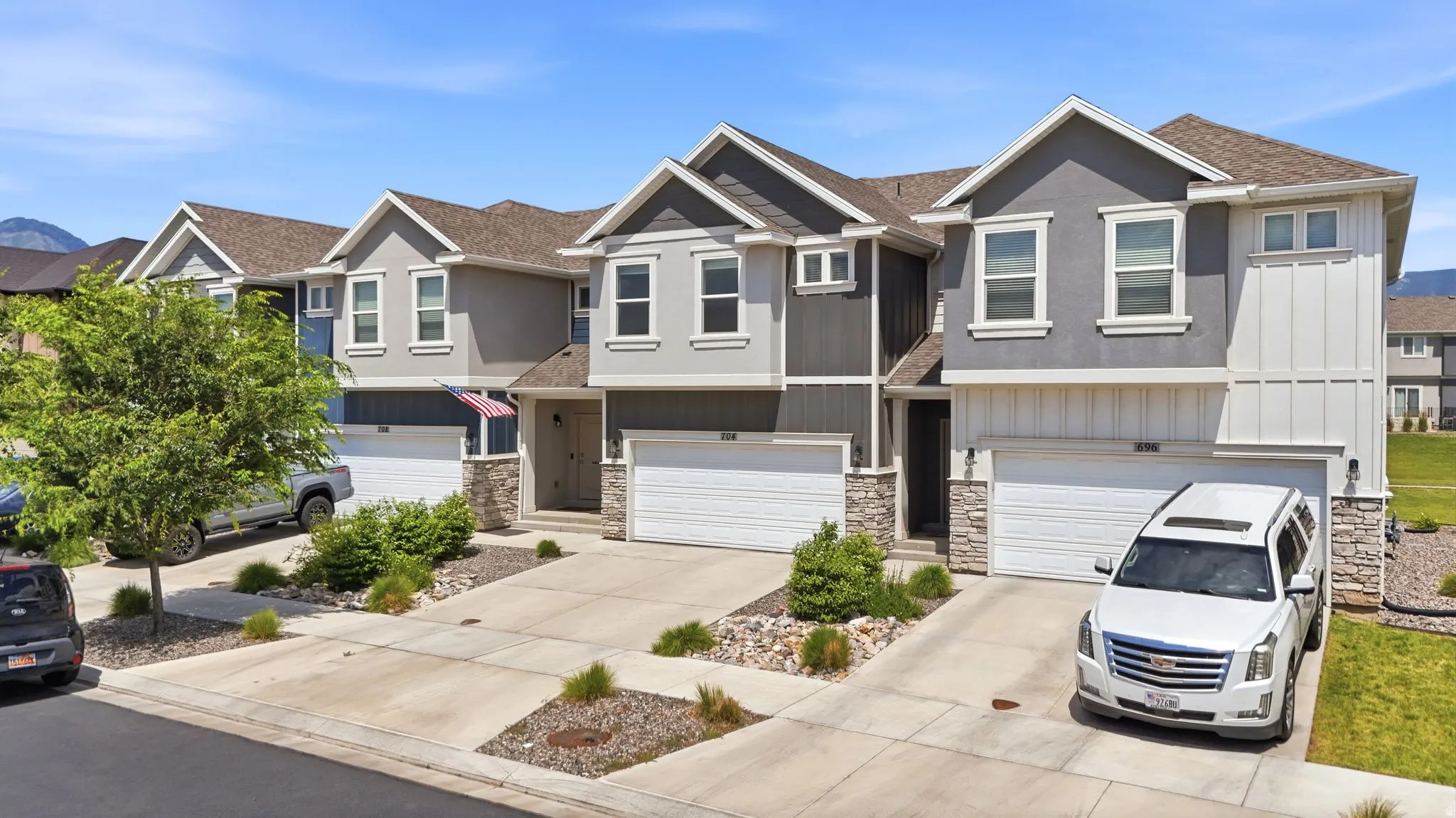 Modern multi-family dwelling featuring a gray stucco exterior with white trim, a stone façade accent, and an integrated garage